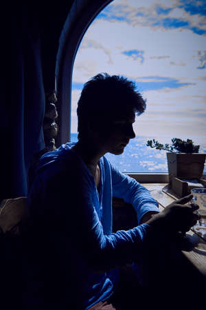 Silhouette of a young man finishing a cappuccino against the background of a window with a view of...