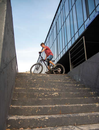 Russia, Moscow, September 2020. A teenager with a Bicycle stands at the top of the stairs at the glass building.のeditorial素材