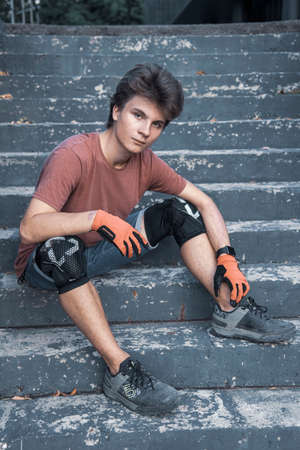 A teenager wearing knee pads , Cycling gloves and boots sits on a step on a warm summer day.のeditorial素材