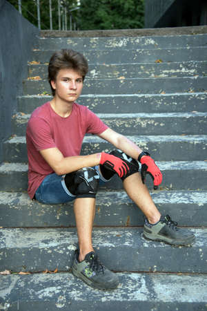 A teenager wearing knee pads , Cycling gloves and boots sits on a step on a warm summer day.のeditorial素材