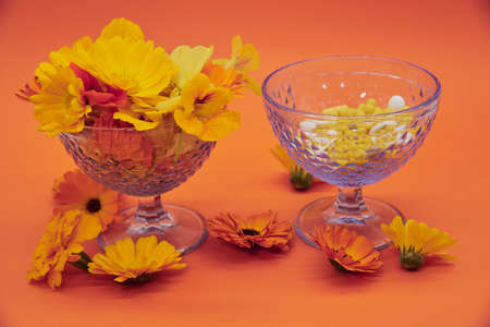 Bright orange flowers in a blue vase And various tablets and pills in another vase on an orange background. Copy space for text, design.の写真素材