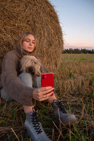 A girl and a dog take a selfie on their phone in a field near a haystack.の写真素材