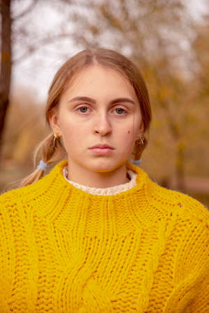 Facial portrait of a blonde girl in a bright warm yellow sweater on a blurry background of nature.の写真素材