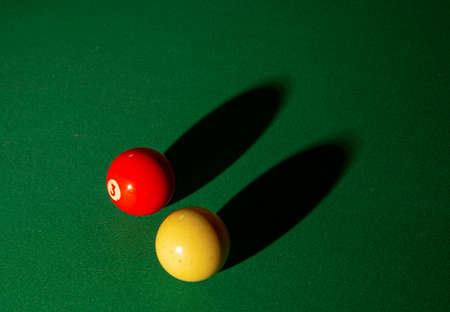 One red billiard ball casts a long black shadow on the table surface.の写真素材