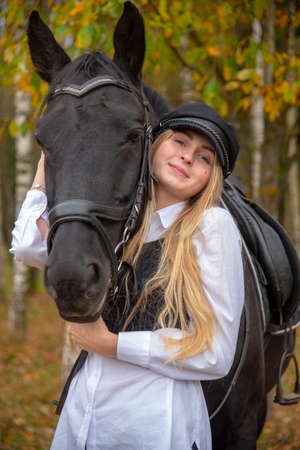 portrait of a girl with blonde hair and a Bay horse on the background of an autumn forest.の写真素材