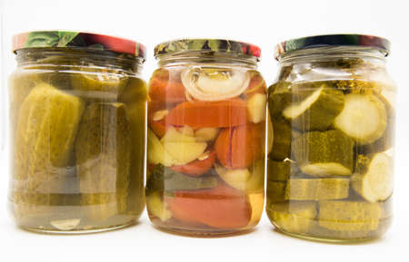 Three transparent jars with pickled vegetables, cucumbers, tomatoes and peppers, on a white background.の写真素材