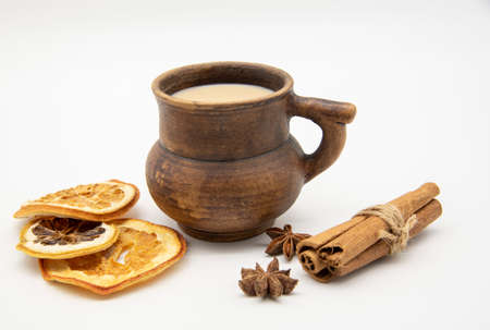 Brown clay mug with drink, cinnamon sticks and star anise on a white background.の写真素材