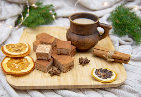 A clay mug with a drink and various Goodies are on a wooden tray, standing on a knitted blanket. It...
