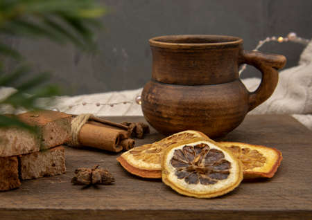 A brown ceramic mug, sweets and aromatic spices stand on a wooden tray against a gray wall, decorated with a Christmas garland.の写真素材