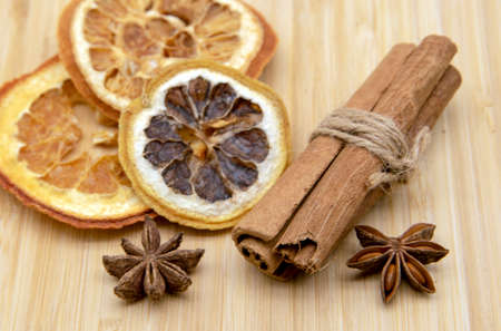 Cinnamon sticks, star anise, and dried oranges lie on a wooden tray.の写真素材
