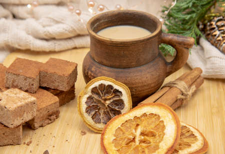 A brown ceramic mug, sweets and aromatic spices stand on a wooden tray, decorated with a Christmas garland.の写真素材