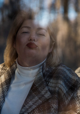 Portrait of a plump middle-aged woman with blonde hair, taken through the window of a cafe, which reflects the bare autumn trees.の写真素材