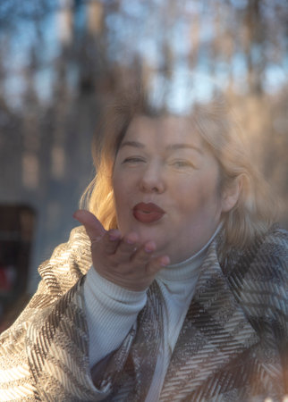 Portrait of a plump middle-aged woman with blonde hair, taken through the window of a cafe, which reflects the bare autumn trees.の写真素材