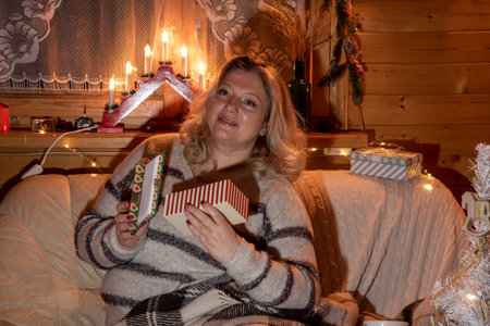 A beautiful plump middle-aged woman with blonde hair sits on a leather sofa in a room decorated for new year's celebrations.の写真素材