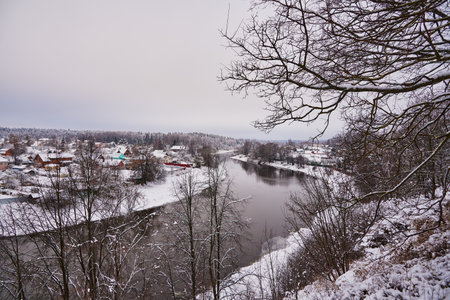 Snow-covered village with colorful wooden houses on the banks of the river, in a cloudy winter day.の写真素材
