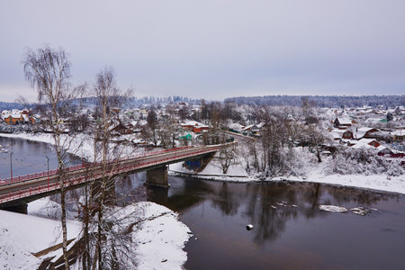 Winter rural landscape. A snow-covered village on the Bank of a river that is crossed by a road bridge.の写真素材