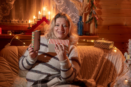 A beautiful plump middle-aged woman with blonde hair sits on a leather sofa in a room decorated for new year's celebrations.の写真素材