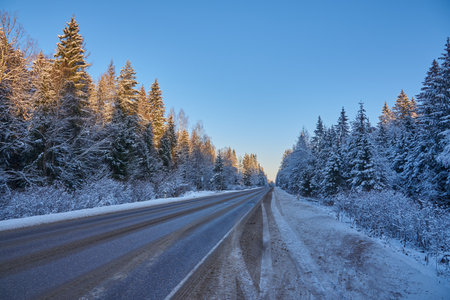 Car paved road in the middle of a snow-covered forest under a bright blue sky. Winter landscape.の写真素材