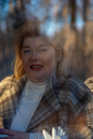 Portrait of a plump middle-aged woman with blonde hair, taken through the window of a cafe, which reflects the bare autumn trees.の写真素材