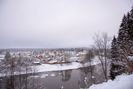 Snow-covered village with colorful wooden houses on the banks of the river, in a cloudy winter day.の写真素材