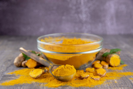 Fresh turmeric root and turmeric powder in a transparent bowl on a gray background. Food supplements, healthy eating.の写真素材