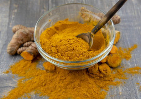 Fresh turmeric root and turmeric powder in a transparent bowl on a gray background. Food supplements, healthy eating.の写真素材