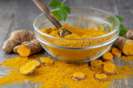 Fresh turmeric root and turmeric powder in a transparent bowl on a gray background. Food supplements, healthy eating.の写真素材