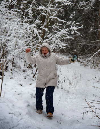 An elderly woman with gray hair in a light jacket on a walk in the winter snow forest.の写真素材