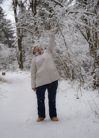 An elderly woman with gray hair in a light jacket on a walk in the winter snow forest.の写真素材