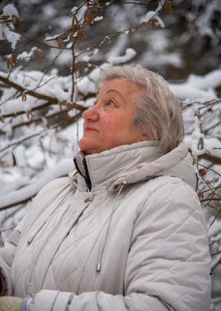 An elderly woman with gray hair in a light jacket on a walk in the winter snow forest.の写真素材