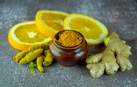 Dry turmeric root, turmeric powder, ginger and citrus on a dark wooden surface.の写真素材