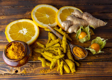 Dry turmeric root, turmeric powder, ginger and citrus on a dark wooden surface.の写真素材