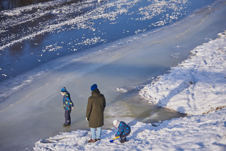 Ruza, Moscow region, Russia, December 2020. Dad with two sons walking on the edge of the ice on the river Ruza. Fragile ice on the river, the risk of falling into icy water. Winter entertainment.のeditorial素材