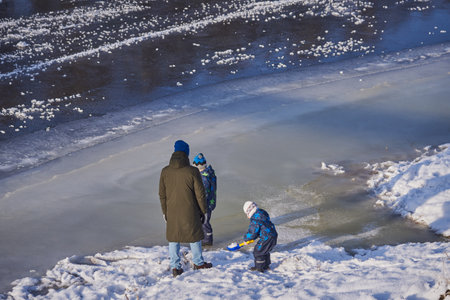 Ruza, Moscow region, Russia, December 2020. Dad with two sons walking on the edge of the ice on the river Ruza. Fragile ice on the river, the risk of falling into icy water. Winter entertainment.のeditorial素材