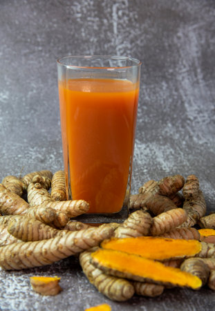 Vitamin bright orange cocktail in a clear glass and fresh turmeric root on a gray table. healthy food supplements.の写真素材