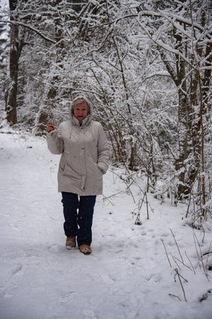 An elderly woman with gray hair in a light jacket on a walk in the winter snow forest.の写真素材