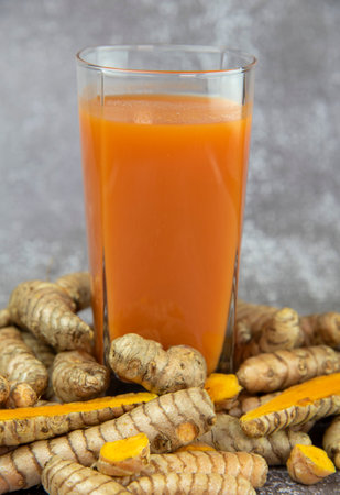 Vitamin bright orange cocktail in a clear glass and fresh turmeric root on a gray table. healthy food supplements.の写真素材