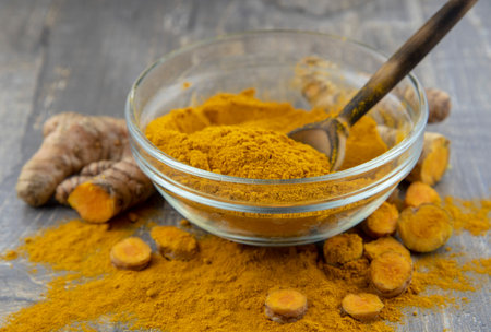 Fresh turmeric root and turmeric powder in a transparent bowl on a gray background. Food supplements, healthy eating.の写真素材