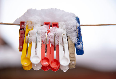 Bright colored clothespins covered with snow on a clothesline.の写真素材