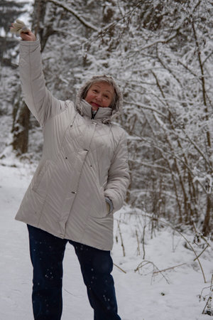 An elderly woman with gray hair in a light jacket on a walk in the winter snow forest.の写真素材