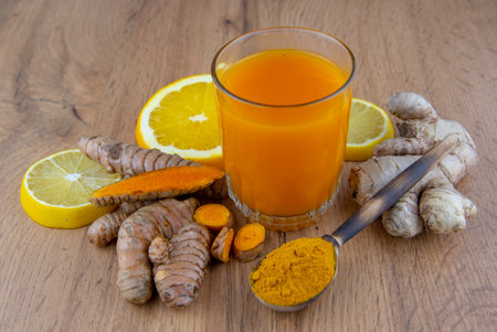 A glass of vitamin cocktail, fresh turmeric root, ginger and orange on a gray background. The...