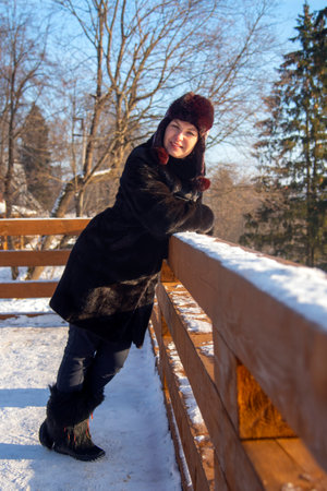 A middle-aged woman with red hair , wearing a black fur coat, against the background of a winter landscape on a sunny day.の写真素材