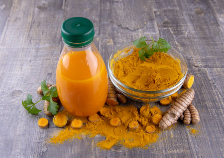 Turmeric powder in a clear bowl, fresh turmeric root and vitamin cocktail in a bottle on a gray background.の写真素材