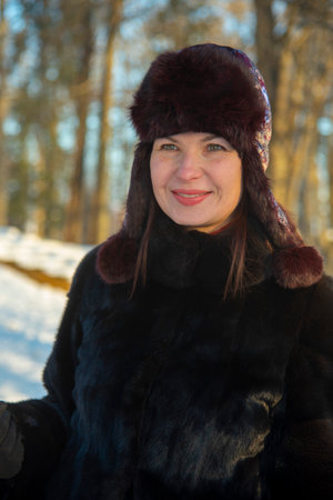 Portrait of a middle-aged woman in a warm hat and fur coat on a sunny winter dayの写真素材