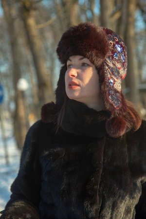 Portrait of a middle-aged woman in a warm hat and fur coat on a sunny winter dayの写真素材