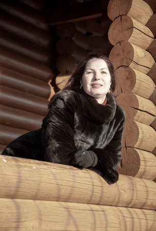 A beautiful 45-year-old woman with red hair poses on the veranda of a log house on a winter day.の写真素材