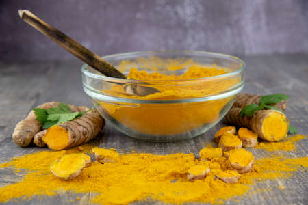 Fresh turmeric root and turmeric powder in a transparent bowl on a gray background. Food supplements, healthy eating.の写真素材