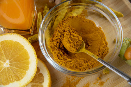 Turmeric powder in a glass bowl and a glass of juice on a light wooden tray.の写真素材