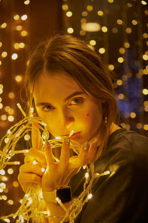Portrait of a beautiful girl with a garland in her hands on a glowing background.の写真素材