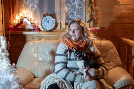 Portrait of a beautiful, plump, middle-aged blonde woman sitting on a sofa with a Chihuahua .の写真素材